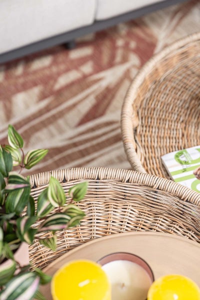 Geflochtene Tabletts aus Korb mit einer Zimmerpflanze und dekorativen Kerzen auf einem gemusterten Teppich.