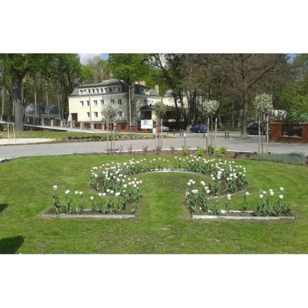 Gepflegter Garten mit Rasenfläche, Blumenbeeten und Gebäuden im Hintergrund