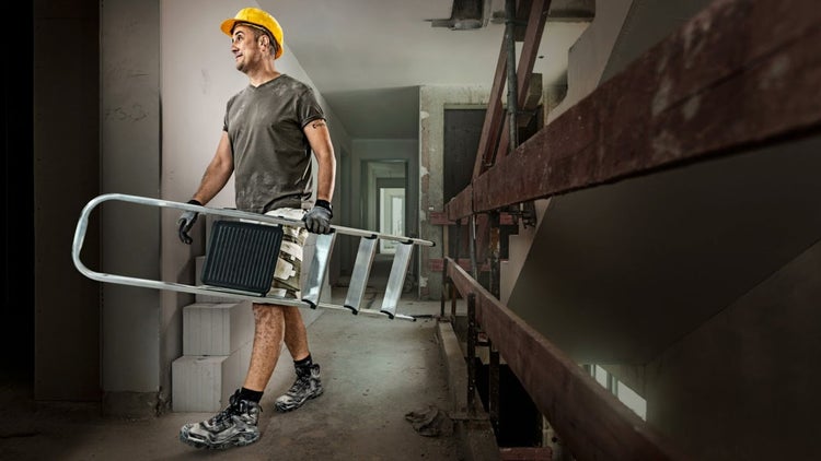 Handwerker trägt eine Aluminiumleiter in einem Gebäude im Rohbau