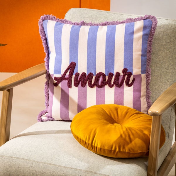 Dekokissen mit Streifenmuster und dem Schriftzug Amour auf einem Sessel, darunter ein rundes Kissen