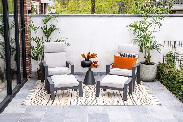 Modernes Gartenmöbel Set bestehend aus zwei Sesseln mit Fußhockern und einem Beistelltisch auf einer Terrasse mit Außenteppich und Pflanzen.