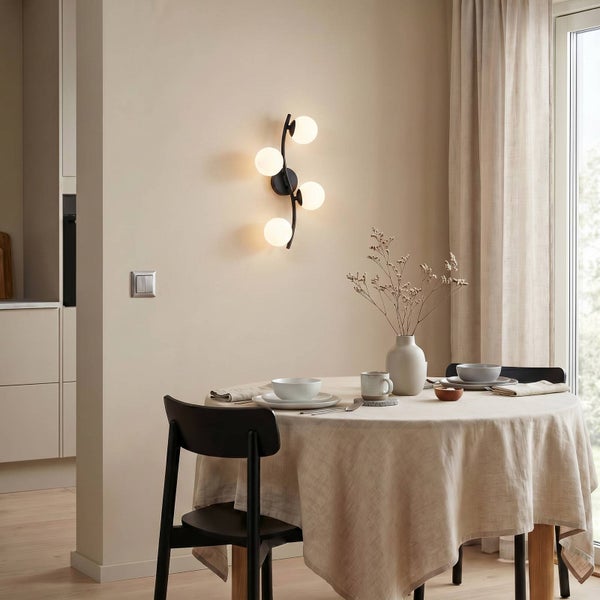 Moderne Wandleuchte mit vier kugelförmigen Glasschirmen an einem schwarzen Metallgestell in einem hellen Esszimmer mit gedecktem Tisch.