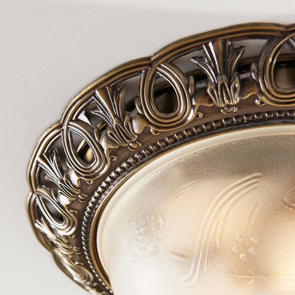 Nahaufnahme einer klassischen Deckenleuchte mit verzierten Metallelementen und mattiertem Glas mit Blumenmuster.
