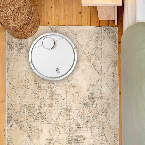 Ansicht von oben auf einen Staubsaugerroboter auf einem Teppich mit geometrischem Muster