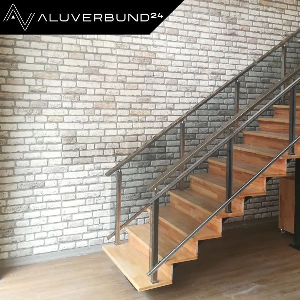 Treppe mit Edelstahlgeländer vor einer Mauer mit Steinmuster