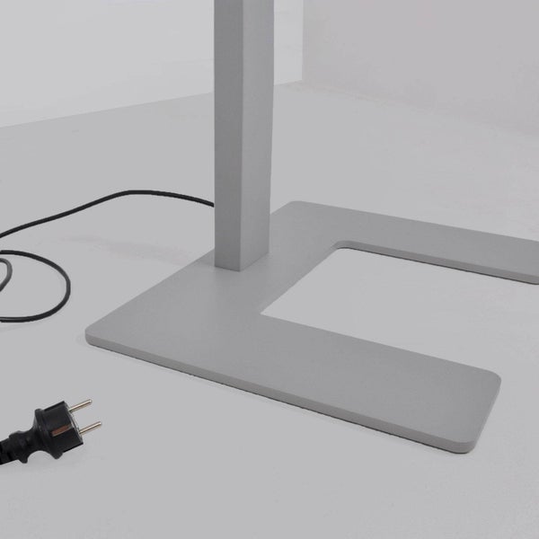 U-förmiger Standfuß einer Stehleuchte mit quadratischem Standrohr, schwarzem Netzkabel und Stecker.