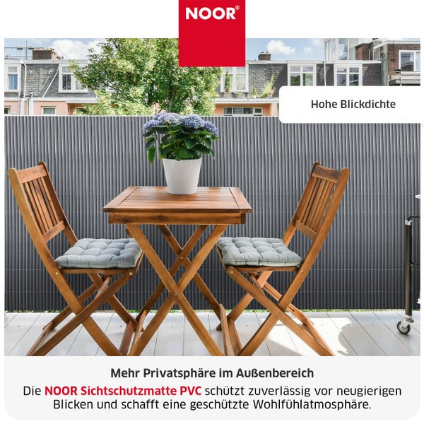NOOR Sichtschutzmatte aus PVC als Balkonverkleidung sorgt für Privatsphäre mit zwei Holzstühlen und einem Tisch auf einem Balkon.