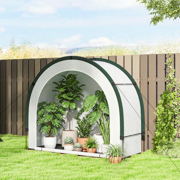 Kleines bogenförmiges Folien-Gewächshaus im Garten, gefüllt mit Topfpflanzen, auf Rasen vor einem Holzzaun.