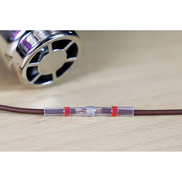 Lötschrumpfverbinder zur Verbindung von zwei Kabeln, Heißluftpistole im Hintergrund.