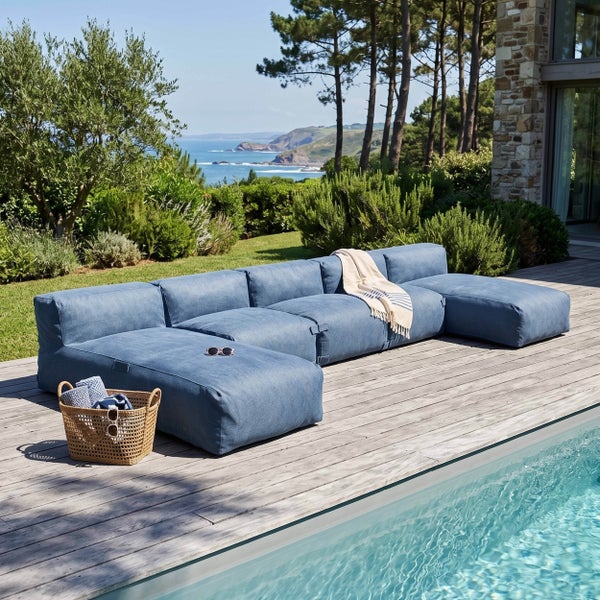 Modulares blaues Outdoor-Lounge-Sofa in U-Form auf einer Holzterrasse neben einem Pool mit Meerblick.