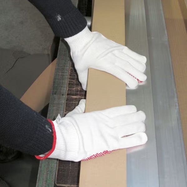 Eine Person trägt Montagehandschuhe bei der Arbeit an einer Abkantmaschine, um Metall oder Paneele präzise zu biegen.