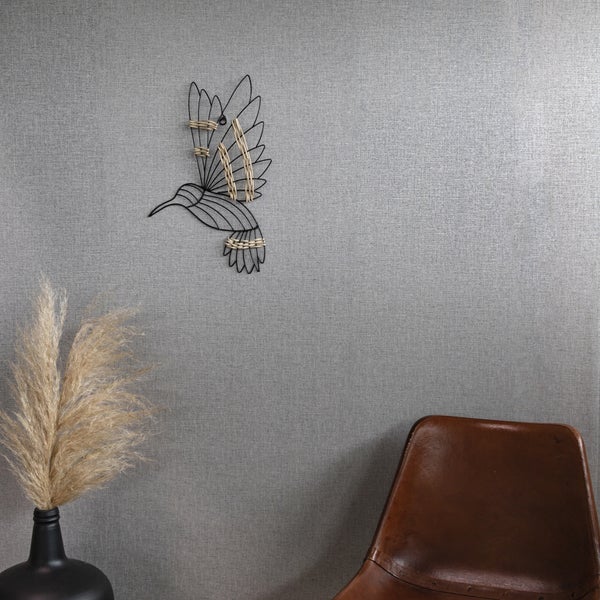 Wanddekoration Kolibri aus schwarzem Metalldraht mit Rattan-Akzenten an einer grauen Wand über einem Sessel und einer Vase.
