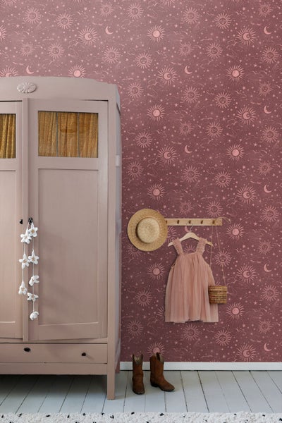 Tapete mit Sonnen-, Mond- und Sternenmuster in einem Kinderzimmer neben einem Vintage-Kleiderschrank und einer Garderobe mit Hut und Kleid.