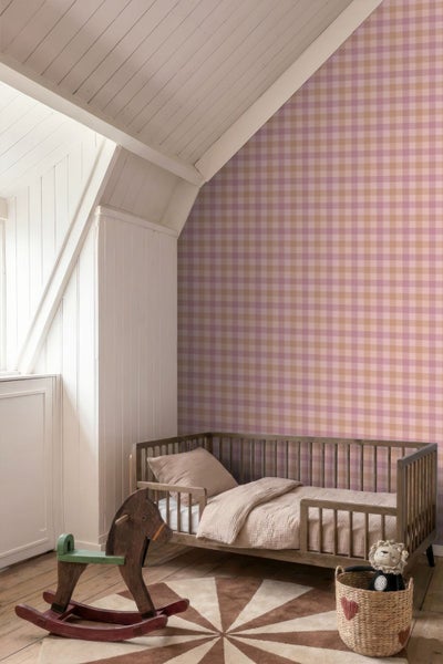 Hell eingerichtetes Kinderzimmer mit Gingham-Tapete, Kinderbett aus Holz, Schaukelpferd und rundem Teppich unter einer Dachschräge.