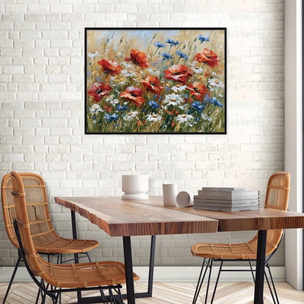 Wandbild mit Blumenwiese im schwarzen Rahmen über einem Holztisch mit Korbstühlen vor einer weißen Backsteinwand.