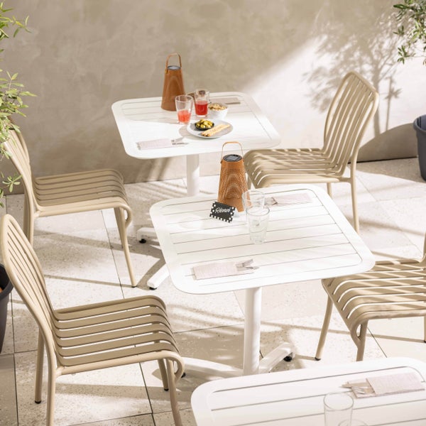Moderne Bistro-Garnitur für den Außenbereich mit weißen, quadratischen Tischen in Latten-Optik und beigen Metallstühlen auf einer hellen Terrasse.
