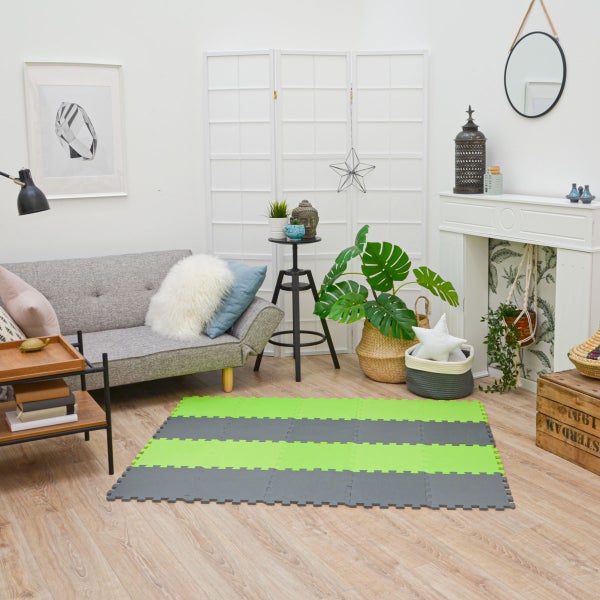 Hell eingerichtetes Wohnzimmer mit grauem Sofa und einer grün-grauen Puzzlematte aus Schaumstoff auf einem Holzboden.