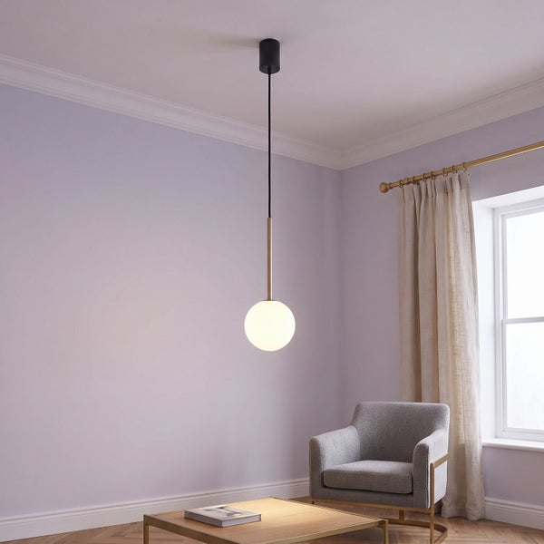Moderne Pendelleuchte mit runder Glaskugel in einem stilvoll eingerichteten Wohnzimmer mit Sessel und Couchtisch.