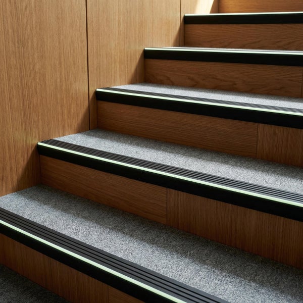Treppenstufen mit Antirutschprofilen und nachleuchtenden Leuchtstreifen auf Holztreppe mit textilen Belägen.