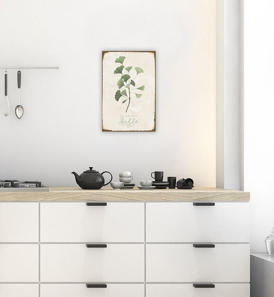 Blechschild mit Ginkgo-Motiv und Schriftzug in einer modernen Küche über einer Arbeitsplatte mit Teekanne und Geschirr.
