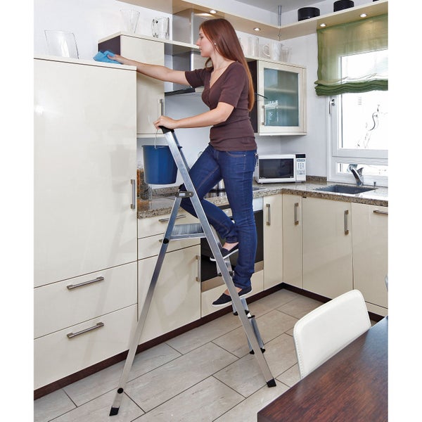 Frau auf einer Aluminium-Trittleiter beim Putzen in einer Küche