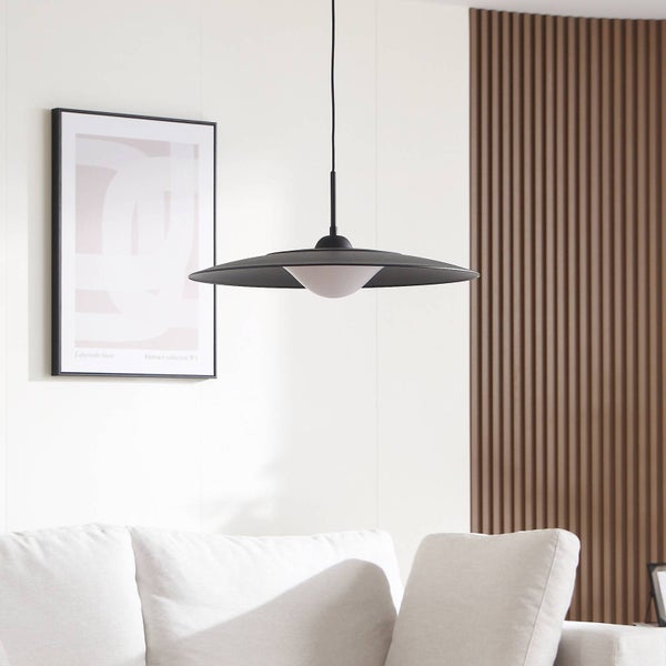 Moderne Pendelleuchte mit flachem schwarzem Schirm und weißem Diffusor in einem hellen Wohnzimmer mit Holzpaneelen und weißem Sofa.