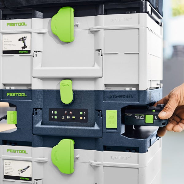 Festool Systainer-Ladestation mit Akku, der von einer Hand in das Ladefach eingeschoben wird, gestapelt mit anderen Systainern.