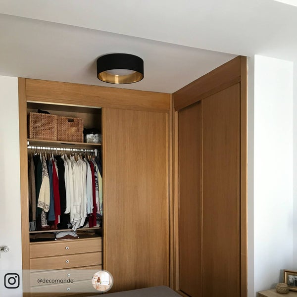 Heller, organisierter Raum mit einem hölzernen Einbauschrank mit Schiebetüren und einer modernen, runden Deckenleuchte in Schwarz und Gold.