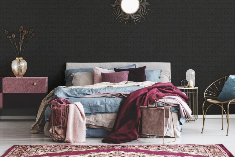 Schlafzimmer mit Bett, Nachttisch, Sessel und dunkler gemusterter Tapete