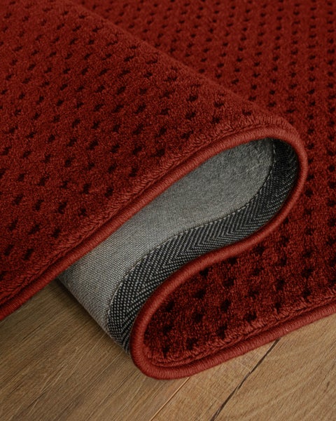 Roter Teppich mit strukturierter Oberfläche und Punktmuster, umgeschlagene Ecke zeigt graue Rückseite, gekettelte Kante.