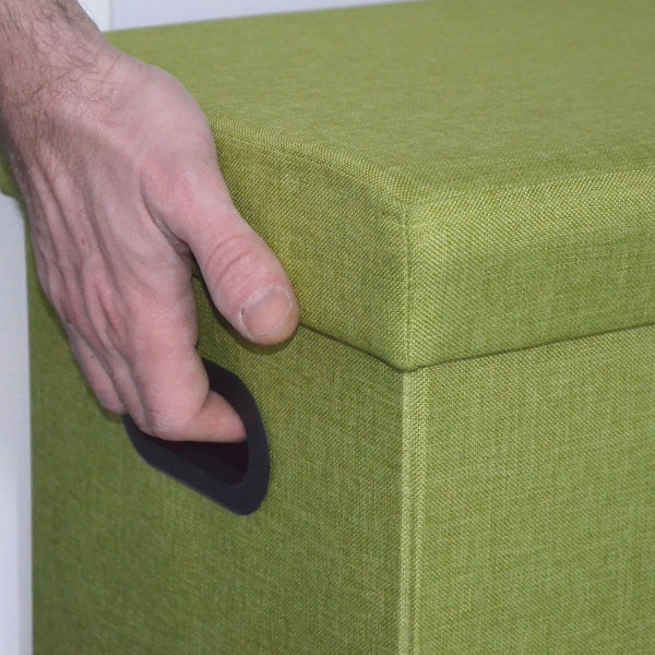 Hand greift in den seitlichen Tragegriff einer grünen Aufbewahrungsbox aus Stoff mit Deckel.