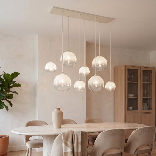Neunflammige Pendelleuchte mit runden Glasschirmen über einem ovalen Esstisch in einem hellen, modern eingerichteten Esszimmer.