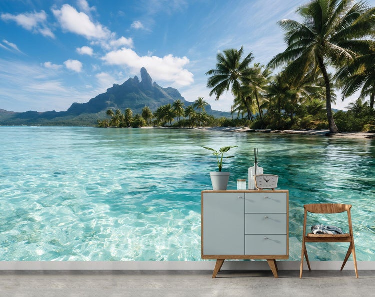 Fototapete mit Tropeninsel Motiv, Berglandschaft mit Palmen und Wasser, dekoriert mit Kommode und Stuhl vor einer Wand.