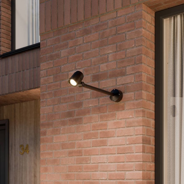 Schwarzer LED-Außenstrahler mit langem Ausleger an einer Backsteinwand montiert. Der Spot ist eingeschaltet und leuchtet.