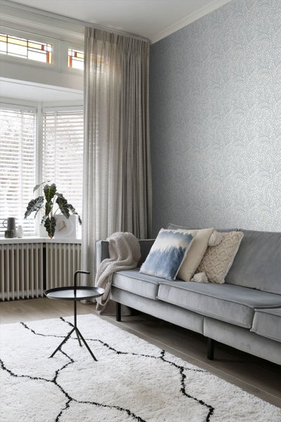 Wohnzimmer mit gemusterter Tapete, Sofa, Teppich und Vorhängen für eine gemütliche Atmosphäre.