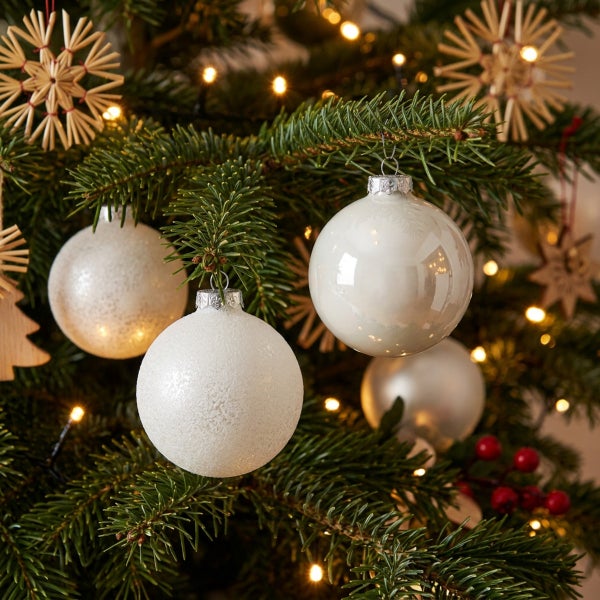 Weihnachtsbaum mit glänzenden und matten Christbaumkugeln sowie Strohsternen und Lichterkette als festliche Dekoration