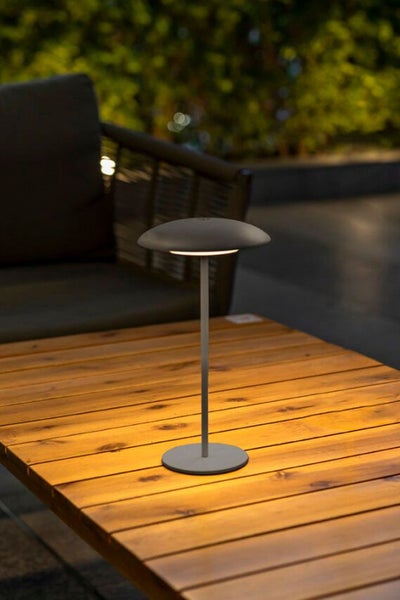 Moderne LED Tischleuchte für den Außenbereich auf einem Holztisch, die eine gemütliche Lichtatmosphäre erzeugt.