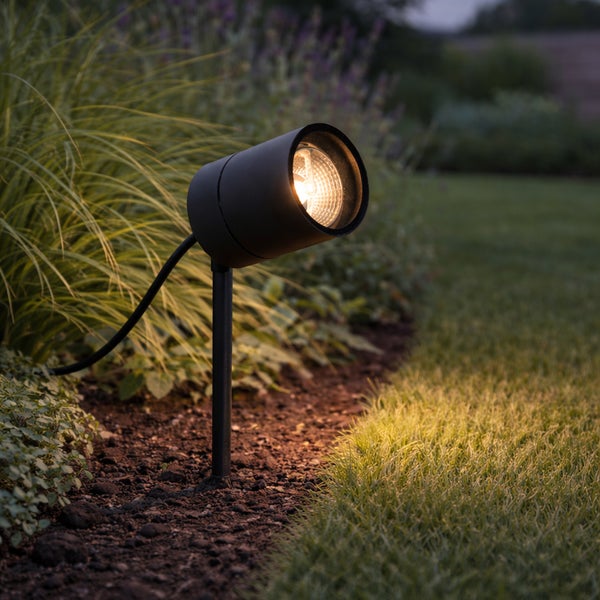 Gartenstrahler mit Erdspieß beleuchtet Pflanzen und Rasen in einem Beet.