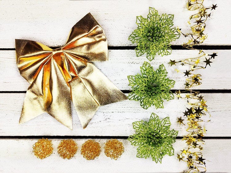 Weihnachtsdekoration Set bestehend aus einer Schleife, drei Blüten, vier kleinen Kugeln und einer Girlande auf weißem Holzuntergrund.
