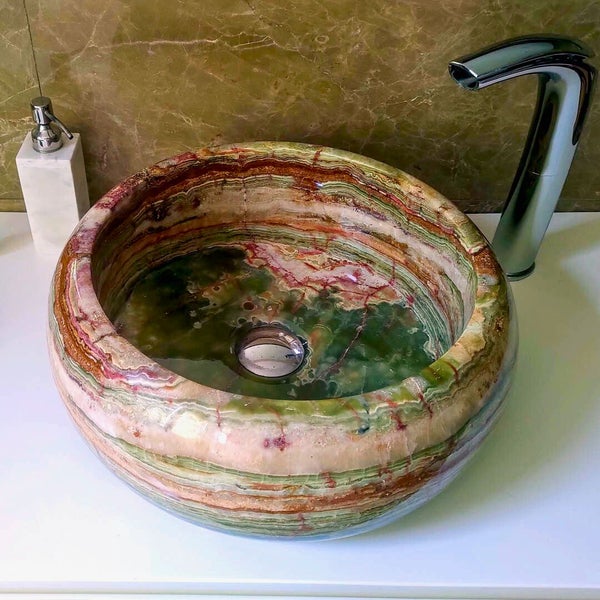 Rundes Aufsatzwaschbecken aus geschichtetem Naturstein mit moderner Waschtischarmatur und Seifenspender in einem Bad.