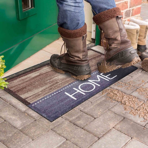 Fußabtreter mit der Aufschrift Home vor einer Haustür mit Stiefeln