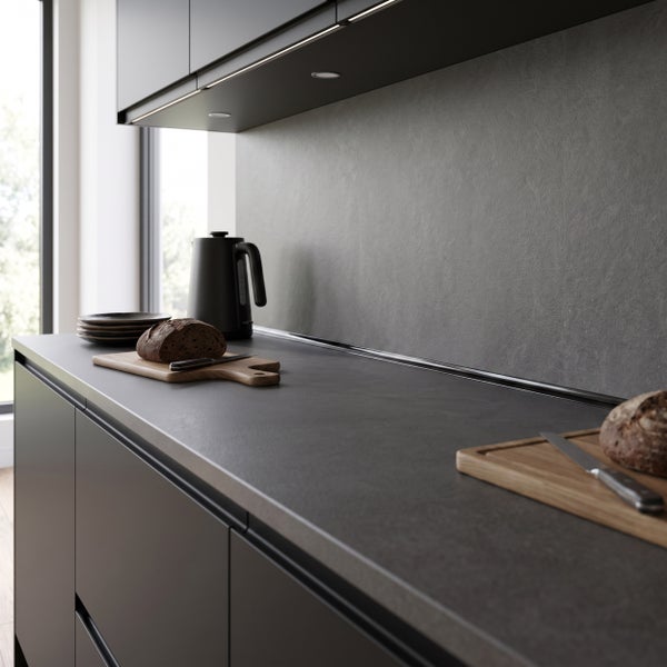 Moderne Küche mit dunkler Arbeitsplatte aus Steinoptik, Hängeschränken mit Beleuchtung, Holzschneidebrettern und einem Wasserkocher.
