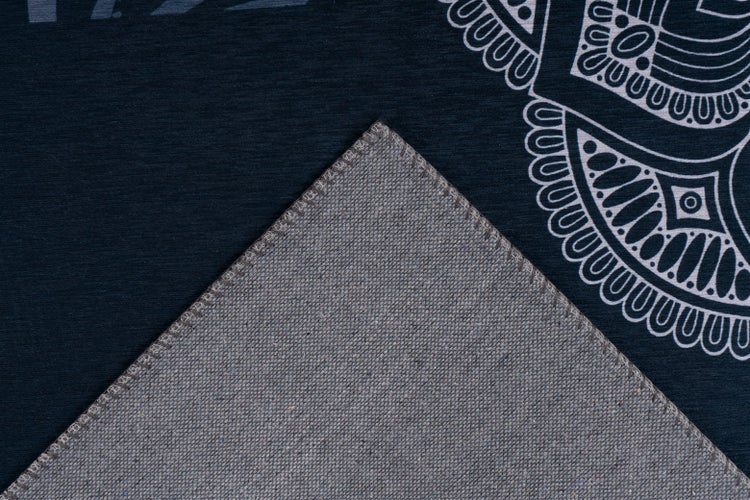Detailaufnahme eines Teppichs mit dunkelblauem Mandala-Muster und grauer gewebter Rückseite mit gesäumter Kante.