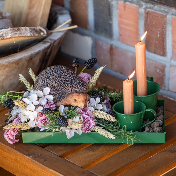 Dekoration mit Kerzen, Blumen, Brombeeren und Igel-Figur auf einem Tablett