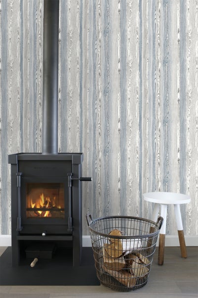 Wohnzimmer mit Kaminofen, Holzkorb und Hocker vor einer Wand mit Holzstrukturtapete