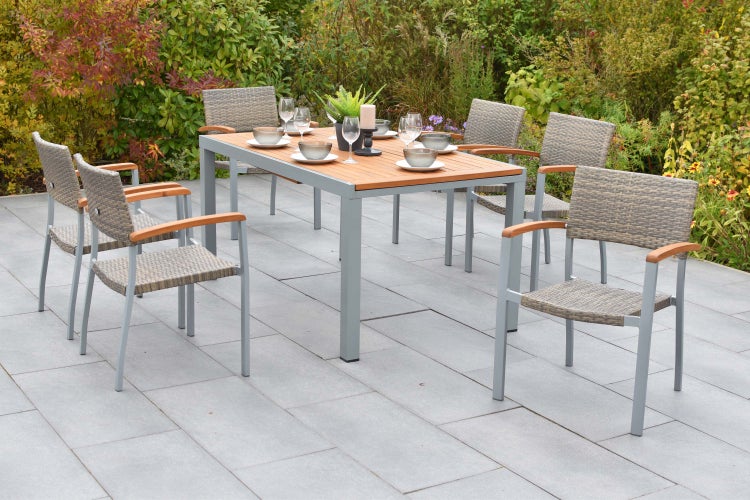Gartenmöbel-Set bestehend aus einem Tisch mit Holzplatte und sechs Stapelstühlen mit grauem Geflecht und Holzarmlehnen auf einer Terrasse.