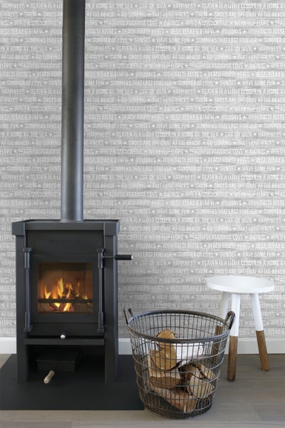 Schwarzer Kaminofen neben einem Korb mit Holz und einem Hocker vor einer gemusterten Wand