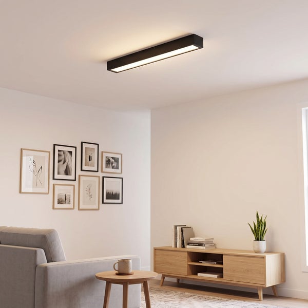 Moderne längliche LED Deckenleuchte in einem wohnlich eingerichteten Wohnzimmer mit hellem Holzmöbel und Bilderwand.