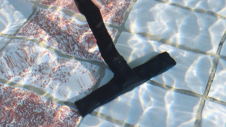 Manueller Bodensauger reinigt einen gefliesten Poolboden unter klarem Wasser.