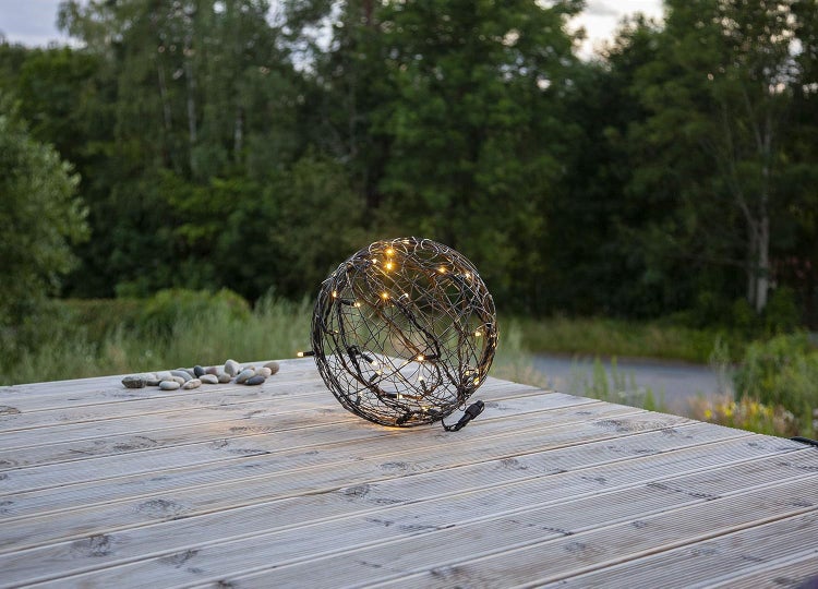 Dekorative Leuchtkugel aus Metall mit warmweißen LEDs auf einer Holzterrasse